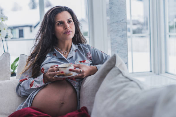 istock Young pregnant woman looking through window. 1128420348