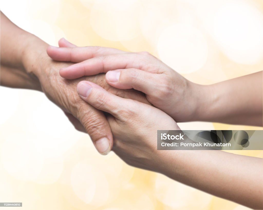Caregiver, carer hand holding elder hand for hospice care. Philanthropy kindness to disabled old people concept with gold bokeh background.Happy mother's day. Hand Stock Photo