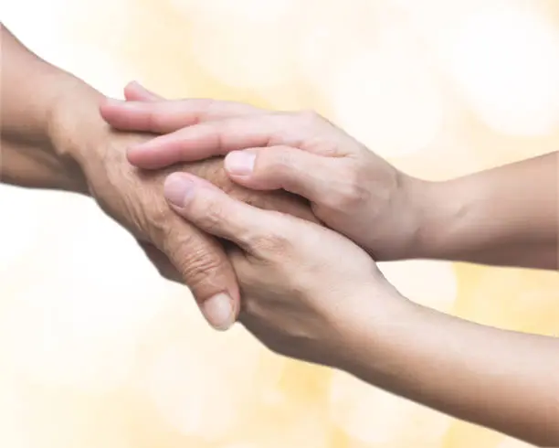 Photo of Caregiver, carer hand holding elder hand for hospice care. Philanthropy kindness to disabled old people concept with gold bokeh background.Happy mother's day.