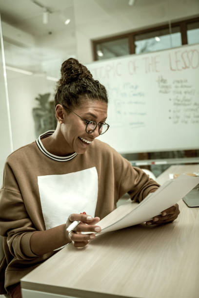 istock Young teacher laughing while reading the essay of her pupil 1128444329