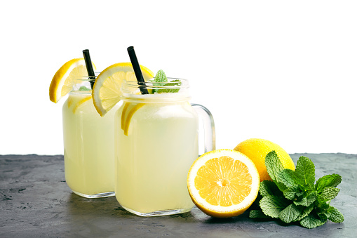 Refreshing lemonade drink with lemon slice and mint in the jar on dark table and white background.