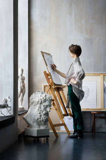 Young successful artist in art workshop studio Modern creative artist sculptor woman female creator student at art studio workshop workplace exhibition with wooden paintbrushes drawings, sketches and gypsum plaster sculptures: horse, male portrait fine art image pictures stock pictures, royalty-free photos & images