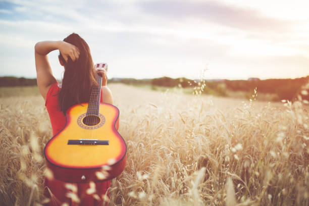 istock Woman walking through the wheat field with guitar on back. 1128450631