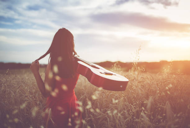 istock Woman walking through the wheat field with guitar on back. 1128450709
