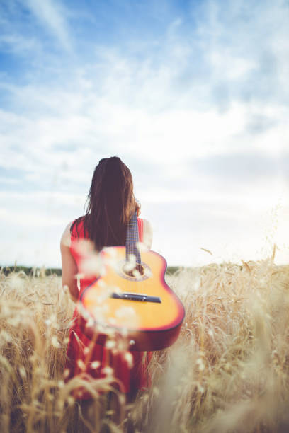 istock Woman walking through the wheat field with guitar on back. 1128450781