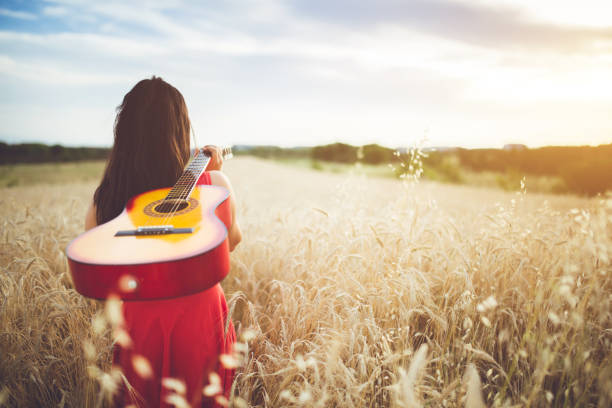 istock Woman walking through the wheat field with guitar on back. 1128450978