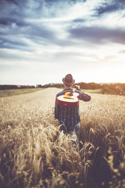 istock Man walking through the wheat field with guitar on back. 1128454911
