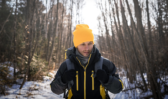 Hiking: A man in a yellow hat goes hiking in a winter forest and carries a large gray backpack. Front view. Portrait.