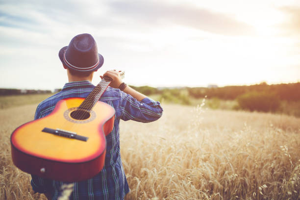 istock Man walking through the wheat field with guitar on back. 1128455038