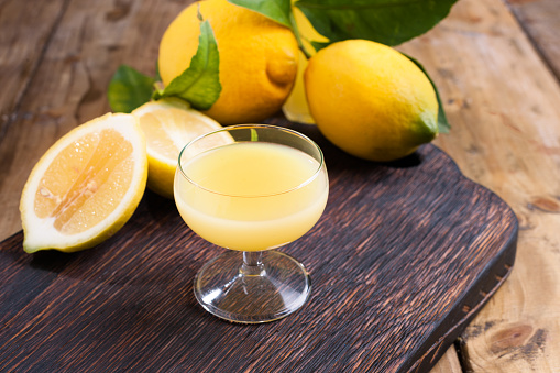 limoncello in a glass and fresh citrus fruits with green leaves. Traditional Italian lemon liqueur. Alcohol on a dark wooden background. Antique drinks from the south.