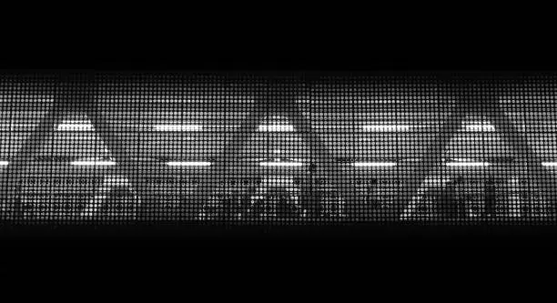 People walking behind a grid in a railway station (black and white)