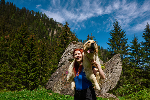hiker woman in sunny day carrying her golden retriever and enjoying time in nature.