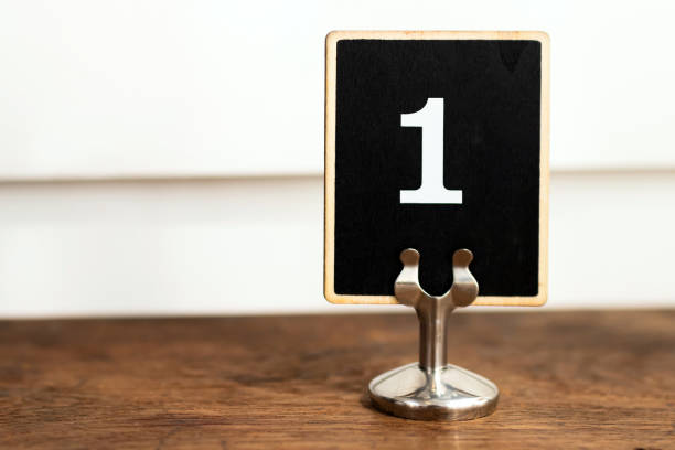 Number one on black label standing on wooden table with white wall on background. stock photo