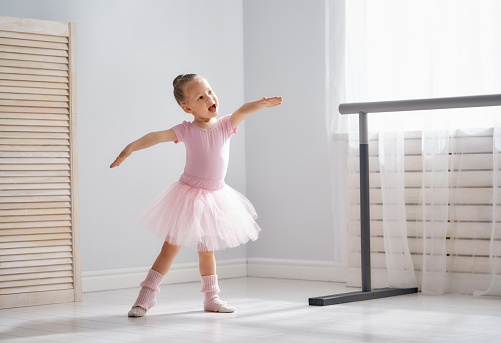 Cute little girl dreams of becoming a ballerina. Child girl in a pink tutu dancing in a room. Baby girl is studying ballet.