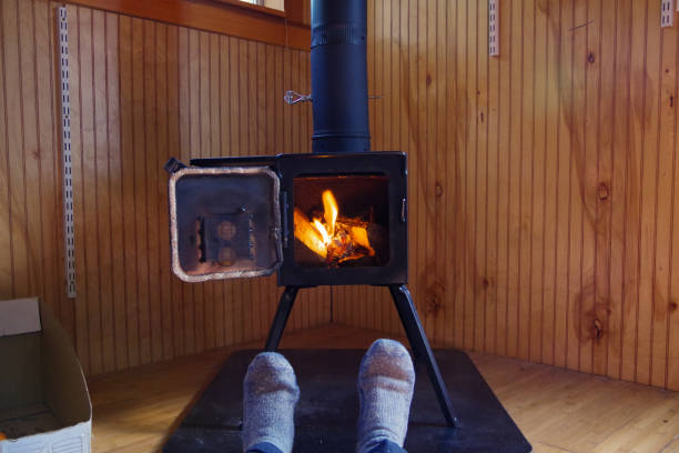 Man's feet in Wool socks relaxing in front of wood stove burning in a cozy tiny house cabin stock photo
