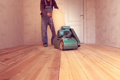 carpenter polishes a wooden floor by electric grinding wood machine in a room