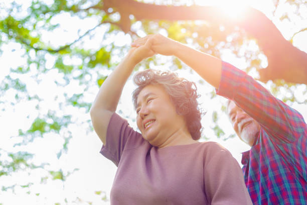 vie heureuse et longue vie concept. vieille femme de femme dansant avec son mari ou le vieil homme au parc sous l’arbre. grand-mère et grand-père sentent le bonheur au moment moment merveilleux avec des visages souriants. - senior adult photograph photography family tree photos et images de collection