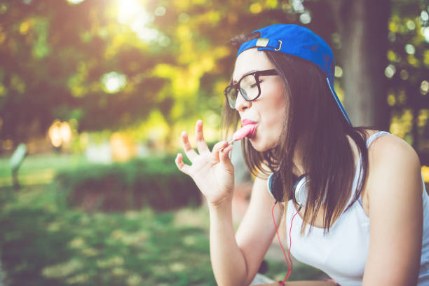 Summer vacation happiness concept. Funny cheerful woman covering eyes with straw hat eating popsicle ice cream orange background