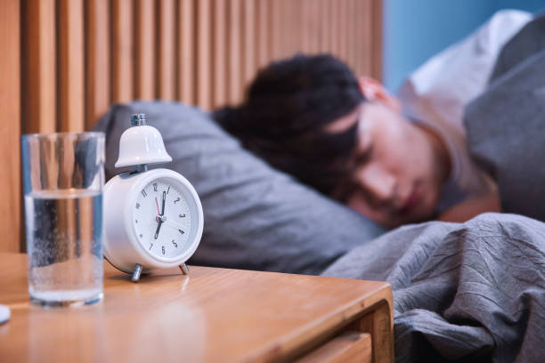 istock Sleepy asian man turning off alarm clock in bed 1128491451