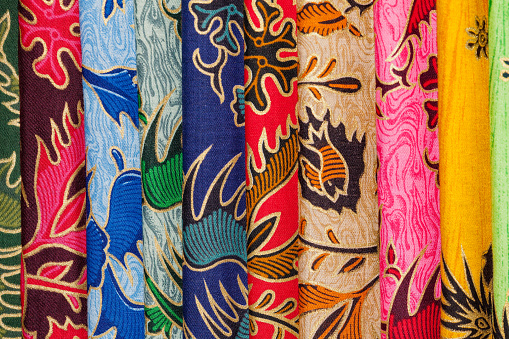 Cheap printed batik textiles at an Indonesian textile market in Ubud. Just the golden outlines are hand painted. Even cheap material has the typical colourful charm of Indonesian fabric. In the social and religious lives of Indonesians textiles are very important. The printed and the more expensive hand painted batik are just two of a large variety of techniques. The symbolism of the various ethnic groups is evident in the variety of textiles. Colour, shapes and their arrangements all have special meanings. Certain designs can only be worn by women or men, or only by the members of the royal family or nobility. Special textiles are worn or exchanged in life cycle or rights of passage ceremonies celebrating birth, circumcision, puberty, marriage, childbearing and death. Textiles play an important role in many traditional events and ceremonies. Among non oil or gas industries the textile and apparel industry is the largest export earner. Ubud, Bali, Indonesia 8°30'26.68\
