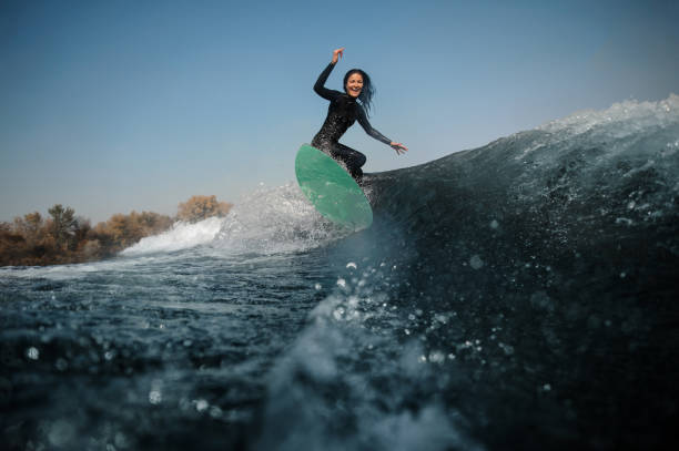 曲げ膝の上緑ウェイク ボードに乗ってブルネットの少女 - women sensuality surfing water sport ストックフォトと画像