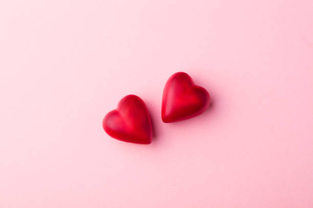 istock Two chocolate heart candies pink pastel paper background. Top view. Copy space. 1128503666