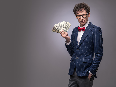 Funny man with fan of money on gray background