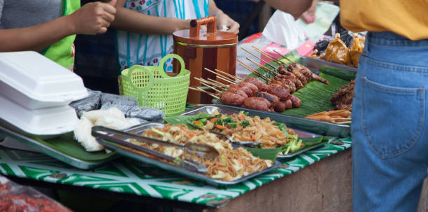 Traditional Thai food market stall selling varieties of street food, fast and comfort food such as pork or chicken skewer, pad thai, sausages. Asian Thai food industry, business and daily life concept mercado de comida tailandesa tradicional puesto de venta variedades de comida rápida de la calle y comida como brocheta de carne de cerdo o pollo, cojín tailandés, salchichas. concepto de vida industria, negocio y diario asiático comida tailandesa