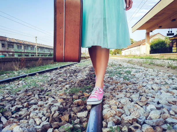 Girl walks the train tracks with a suitcase in hand.