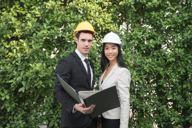 two smiling engineer man and woman holding file and standing on a tree - building contractor engineer digital tablet construction imagens e fotografias de stock