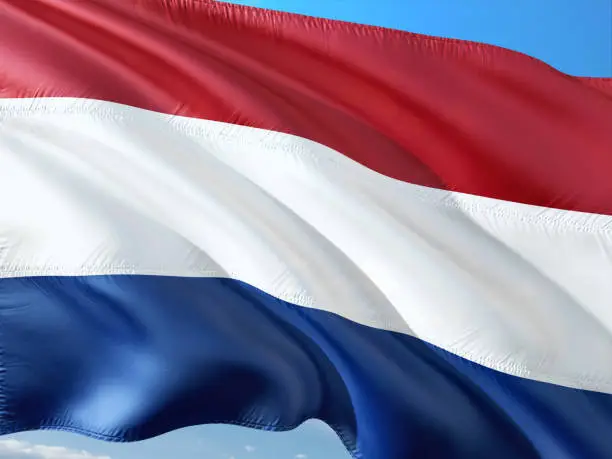 Flag of Netherlands waving in the wind against deep blue sky. High quality fabric.