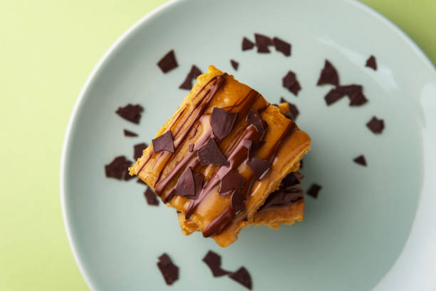 Delicious sweet potato blondies Stack of two sweet potato blondies, thin lines of chocolate and caramel icing running down on the sides, chocolate chips, teal plate, green background - top down view blondy stock pictures, royalty-free photos & images