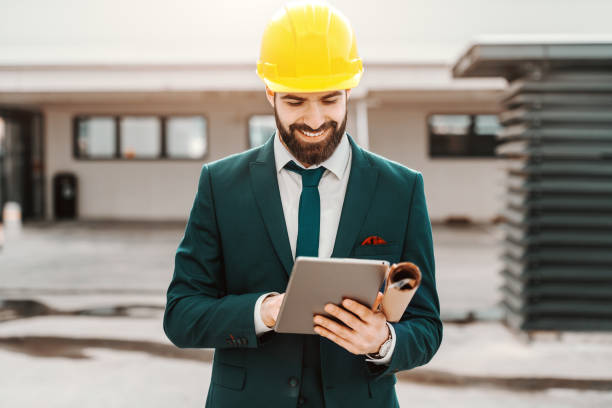 close up of successful architect in formal wear and yellow helmet using tablet. under armpit plans. - building contractor engineer digital tablet construction imagens e fotografias de stock