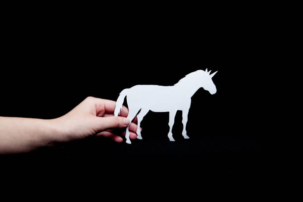 istock A woman's hand holds a white unicorn with a black background paper 1128541772