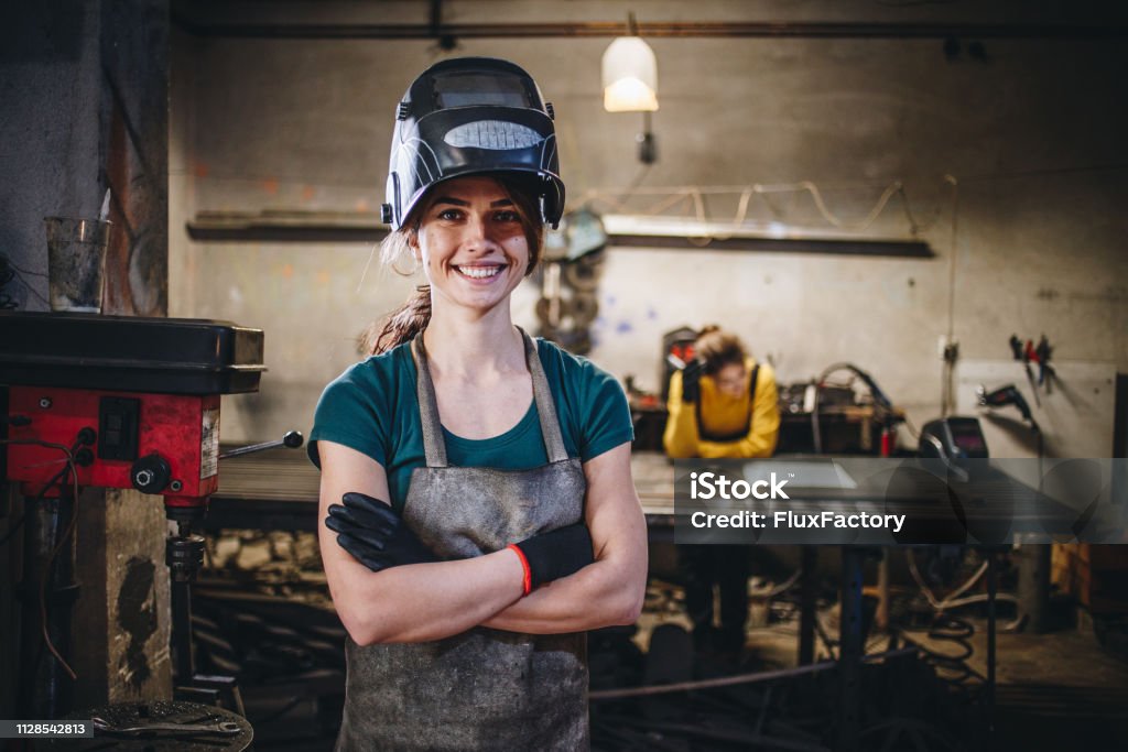 Cheerful girl and her sister in a steel shop Young sisters working in their workshop together, welding and cutting things out of metal. Welder Stock Photo