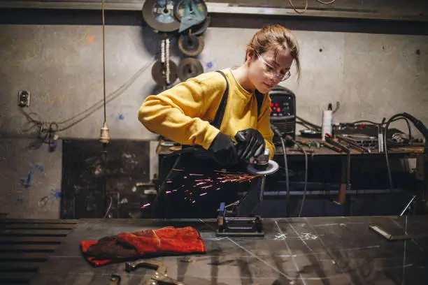 Young girl working at a metal workshop, grinding metal with grinder.
