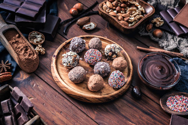 Chocolate truffles and assorted dark chocolate with nuts on rustic old kitchen table Chocolate truffles and assorted dark chocolate with nuts on rustic old kitchen table chocolate truffle making stock pictures, royalty-free photos & images