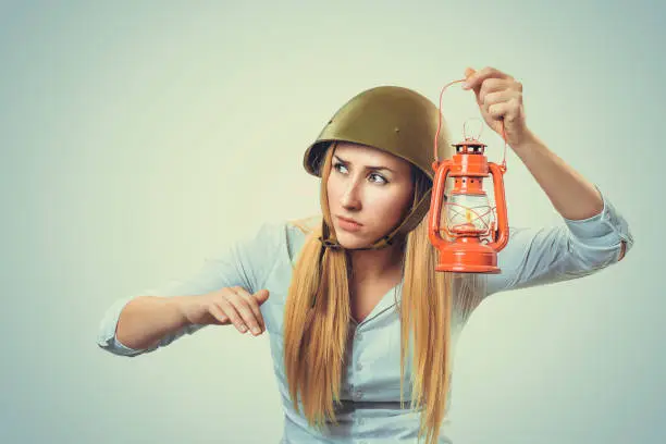 Woman in military armor cap equipment of World War II period holding gaslight searching for friends truth concept. Caucasian person, white formal shirt long blond hair isolated light green background