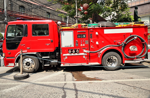 Red fire engine in shift hours parked at Ongpin Street off the Minor Basilica of Saint Lorenzo Ruiz's south wall ready to act against any fire if needed. Binondo District-Chinatown-Manila-Philippines.