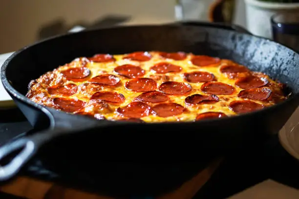 Fesh from the oven deep dish peperoni pizza baked in a large black cast iron skillet. Pepperoni and cheese is glisenting. Extreme close up.