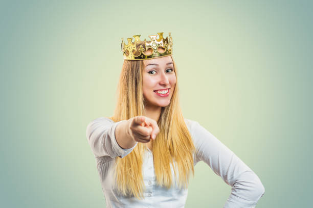 It's you! Portrait happy young girl pointing index finger at you camera smiling happy showing hand gesture this is you It's you! Portrait happy young girl pointing index finger at you camera smiling happy showing hand gesture this is you, pretty woman with golden party crown on head isolated on light yellow green wall beauty queen stock pictures, royalty-free photos & images