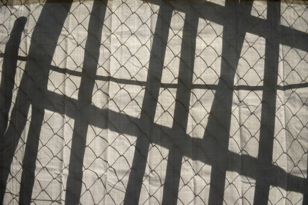 Shadow from behind wire mesh and power line on a construction site white fence.