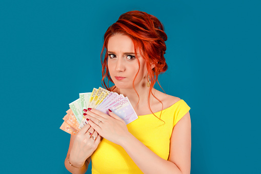 Closeup portrait greedy young corporate employee, woman, holding euro banknotes tight. Negative human emotion facial expression. Financial gain concept. Caucasian person in yellow dress