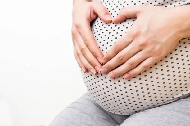 Photo of Happy pregnant woman making heart gesture