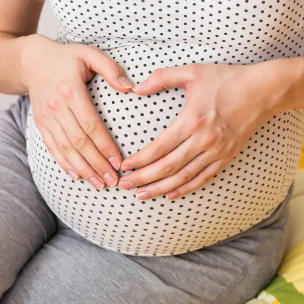 Photo of Happy pregnant woman making heart gesture