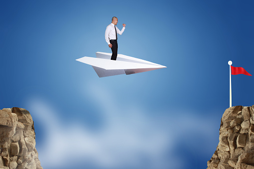 Success vision in business concept. Businessman flying on paper plane across the cliff, conquering adversity with innovation