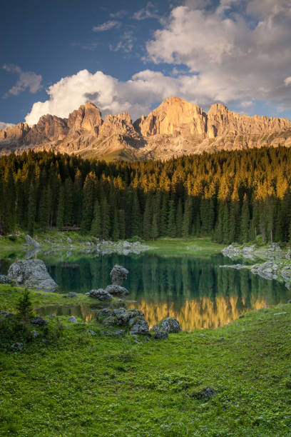 Reflection of the Catinaccio Mountain Group in Lake Carezza The peaks of the Catinaccio illuminated by the last rays of sun and the reflections of the forest in the waters of Lake Carezza albero stock pictures, royalty-free photos & images