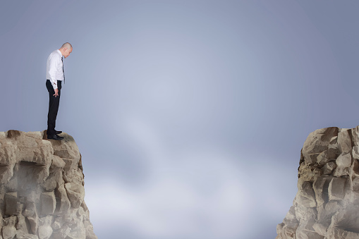 Personal development concept. Future success with risky challenge, businessman standing on the edge of a cliff looking down, afraid worried and confused to conquer adversity and reach business goal target over gap distance