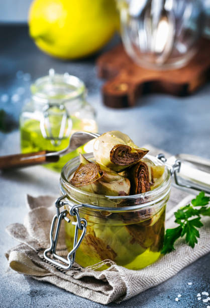 istock Canned artichokes in olive oil, in glass jar with fork, gray kitchen table, selective focus 1128586246