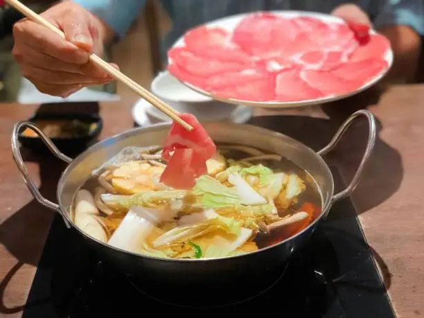 Pork shabu in hand and plate of slice kurobuta pork. Shabu or Sukiyaki hot pot is a Japanese style and Korean style. Rice, sausage and garlic, Delicious shabu shabu in a bowl, healthy food